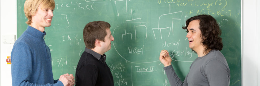 Three researchers stand in front of a blackboard and discuss their results.