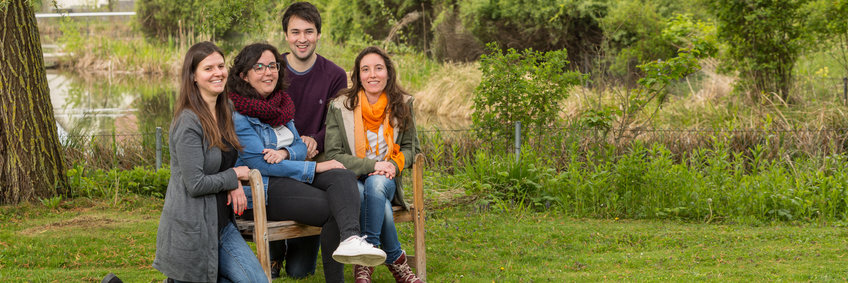 Selection Process for the IMPRS 'From Molecules to Organisms' Four PhD students sit outside by the pond and look into the camera.