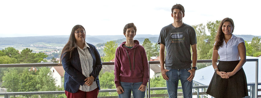 Four PhD students stand on the roof terrace and look into the camera. 